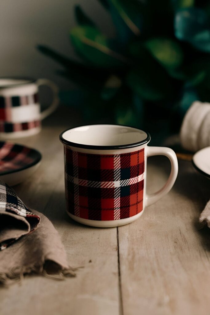 A cozy ceramic mug featuring a classic plaid pattern in warm colors like red and black or green and blue, perfect for autumn or winter