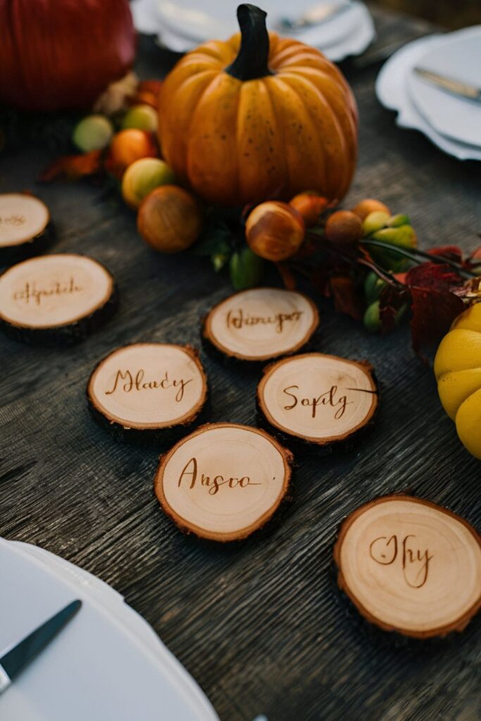 Small wood slices with guests' names burned into them, used as place cards on a fall-themed dining table