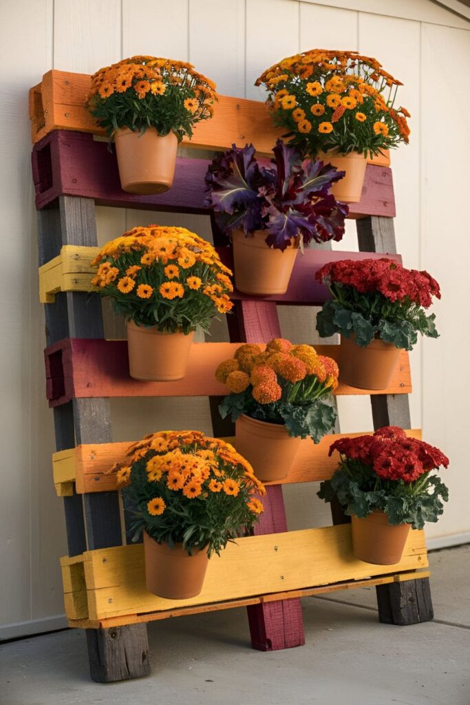 Vertical planter made from a wooden pallet, painted in autumn colors, holding pots of seasonal flowers