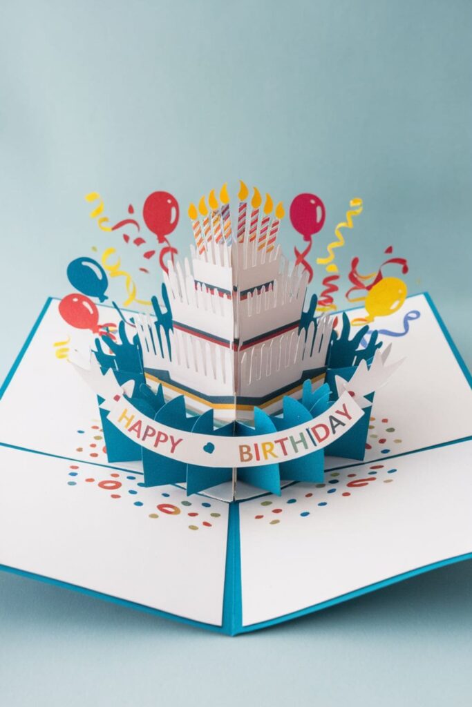 A greeting card opened to reveal a pop-up three-dimensional birthday cake, surrounded by colorful decorations