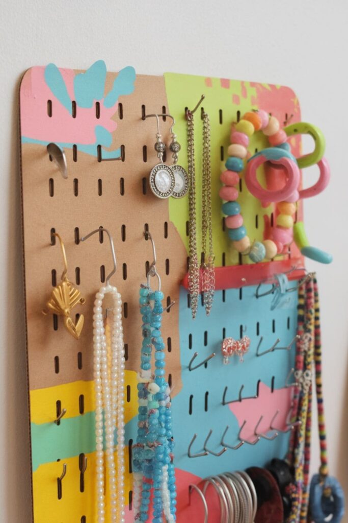 Cardboard jewelry organizer with hooks and pushpins, painted in vibrant colors for hanging earrings, necklaces, and bracelets