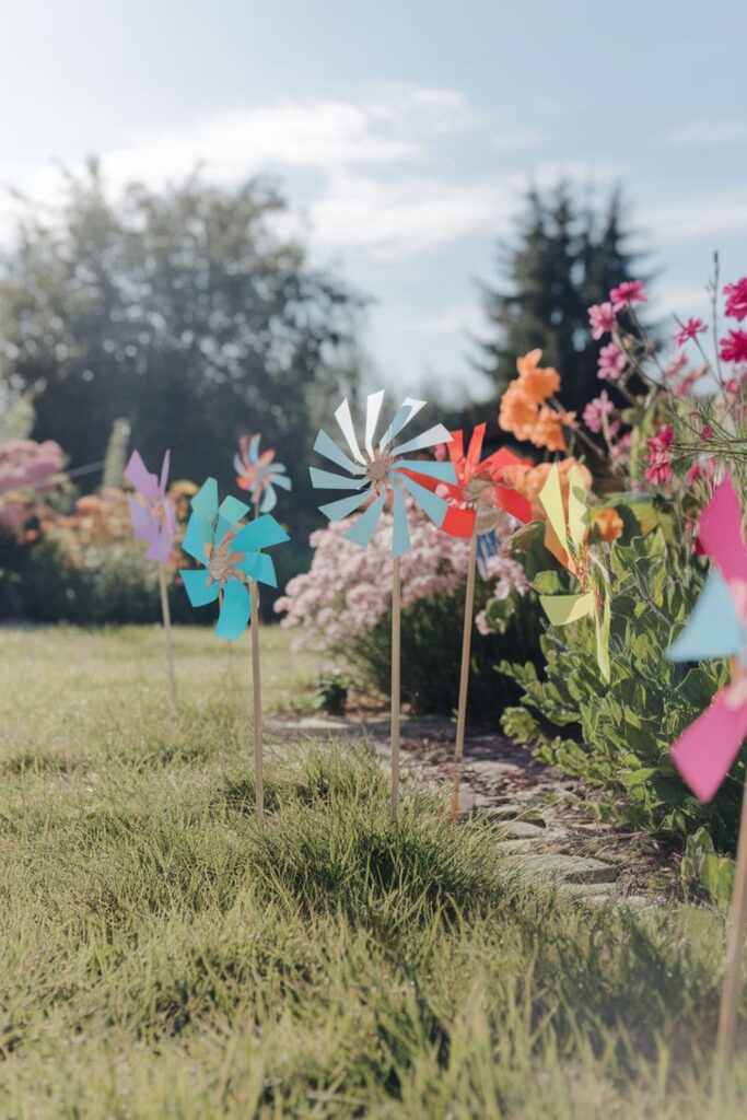 Colorful paper windmills attached to sticks, spinning outdoors in a sunny garden with vibrant flowers in the background