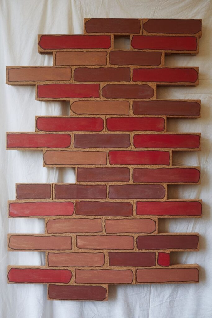 Faux brick wall made from cardboard rectangles painted in red and brown tones, arranged in a staggered brick pattern