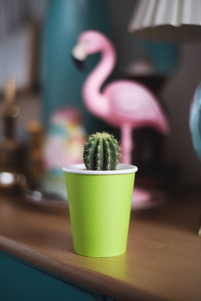 Green paper cups painted to look like cacti with spines drawn on them, placed on a sandy surface with small pebbles