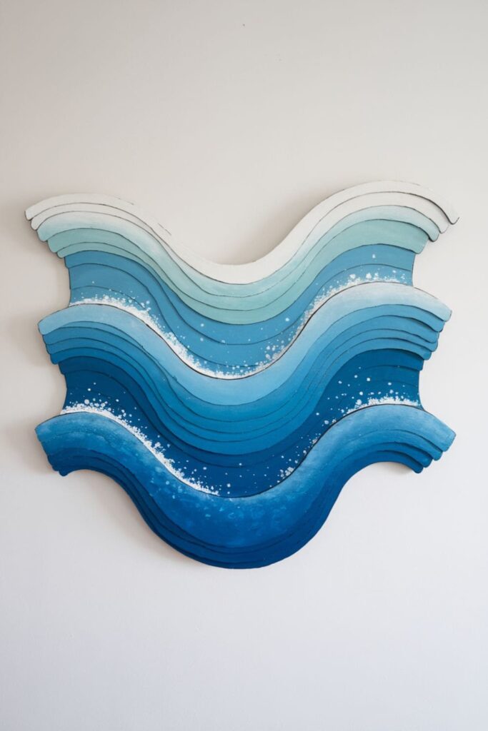 Layered cardboard wall art depicting ocean waves, painted in gradient blues and whites for a serene, beach-inspired effect