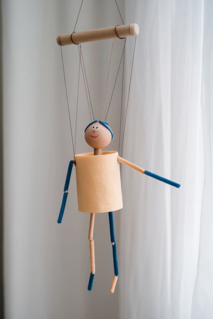 A simple marionette puppet created using half of a paper towel roll as the body, complete with strings and limbs made from craft sticks