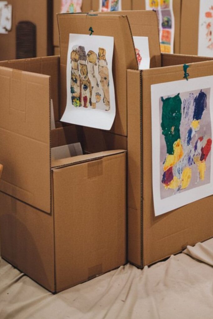 Cardboard art gallery featuring cutout frames displaying children’s artwork, painted white to resemble a real gallery, with kids curating their display