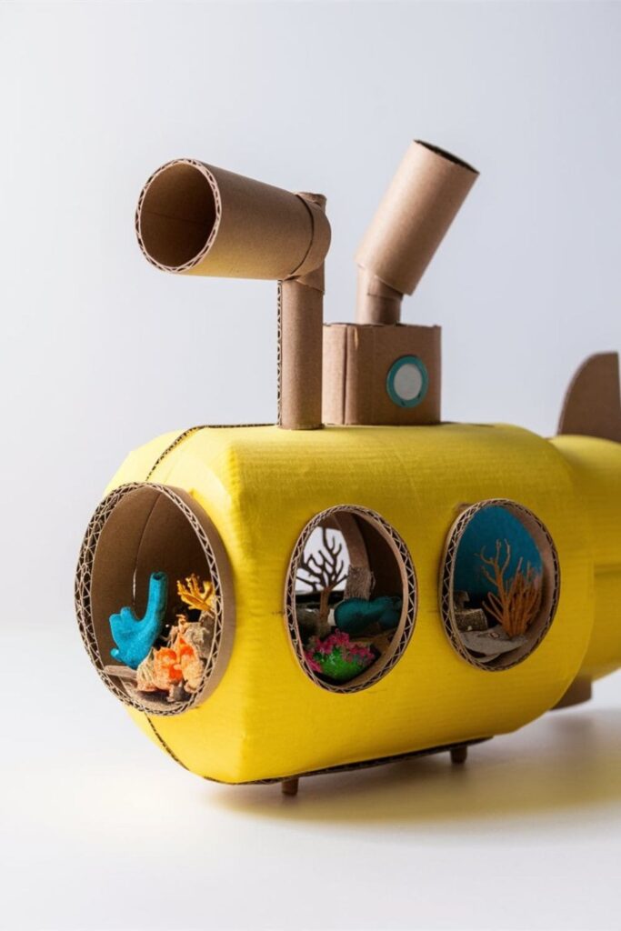 Cardboard submarine painted yellow, featuring portholes, periscopes made from cardboard tubes, and kids pretending to explore underwater