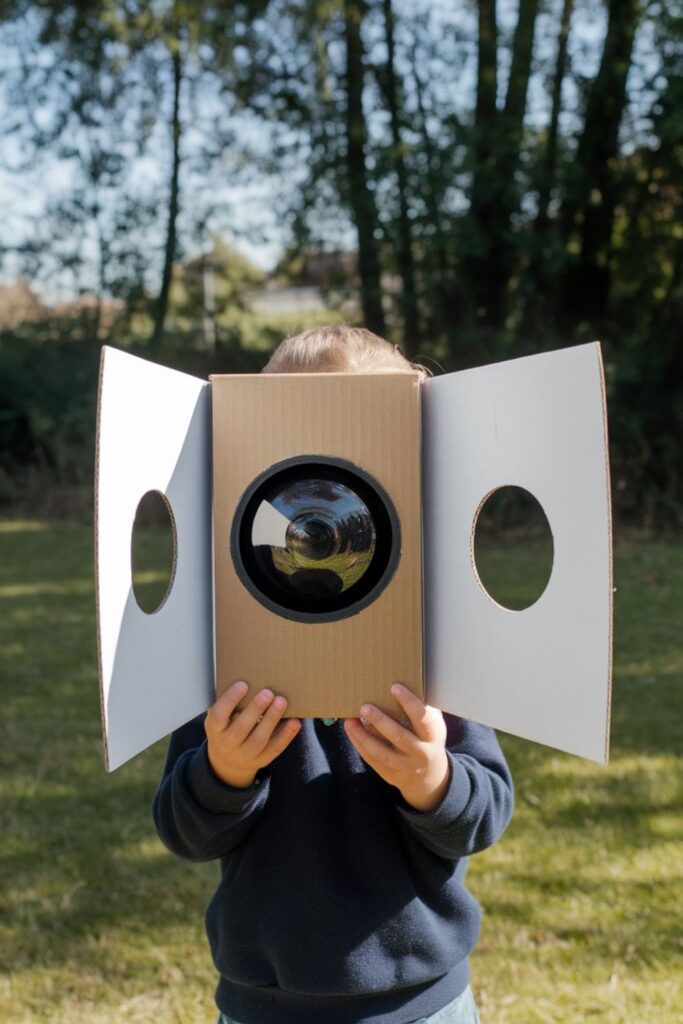 DIY cardboard camera obscura made from a shoebox with holes for light and a white paper screen showing an upside-down reflection