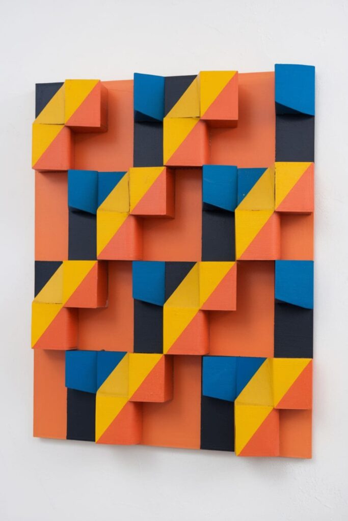 Modern geometric wall art made from painted cardboard roll sections arranged in a repeating pattern on a canvas