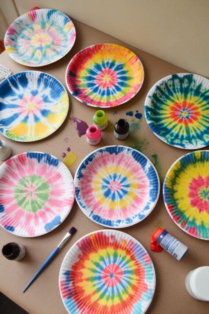 Paper plates with tie-dye patterns created using food coloring and water, drying on a craft table surrounded by supplies