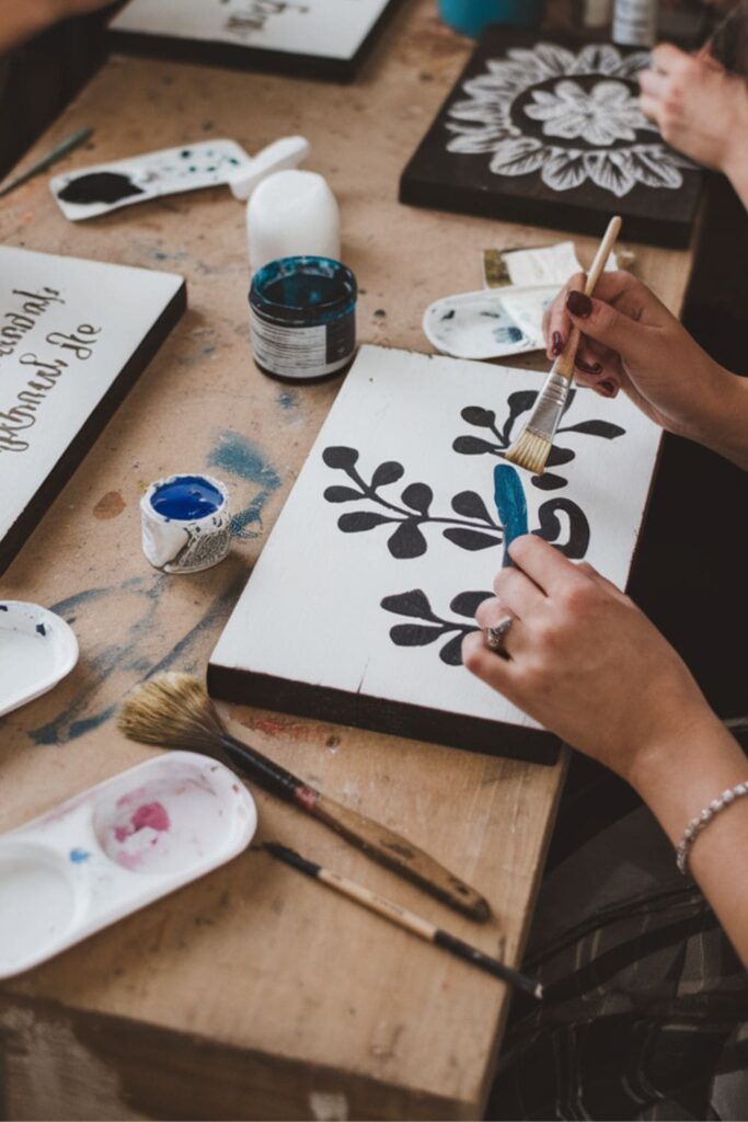 People painting colorful wooden signs with brushes and stencils