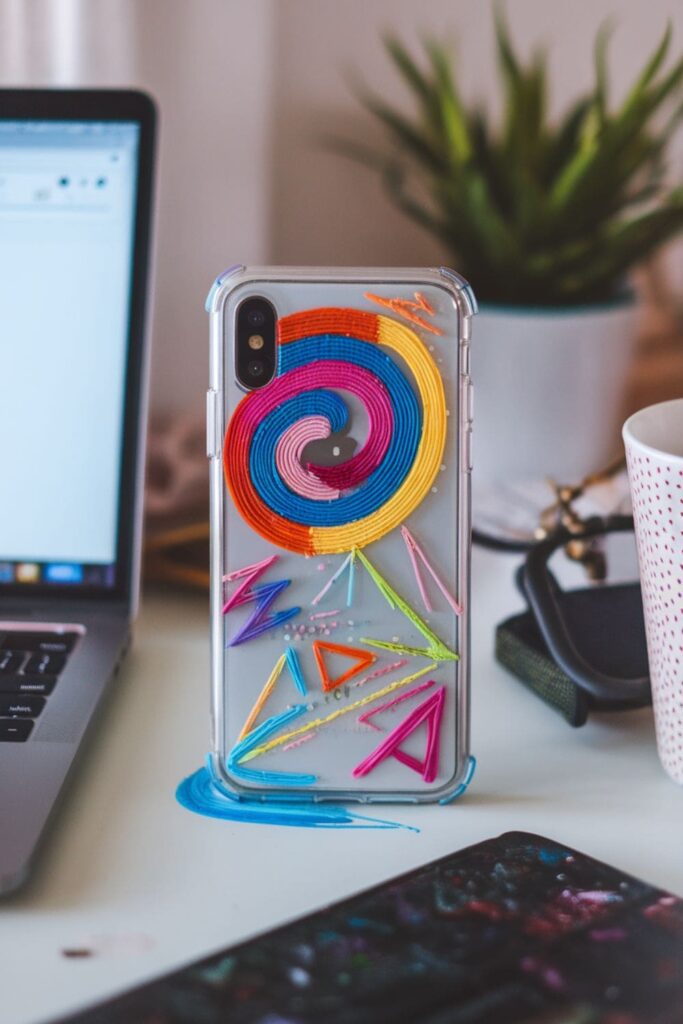 Colorful phone case with hot glue patterns on a table in a cozy workspace